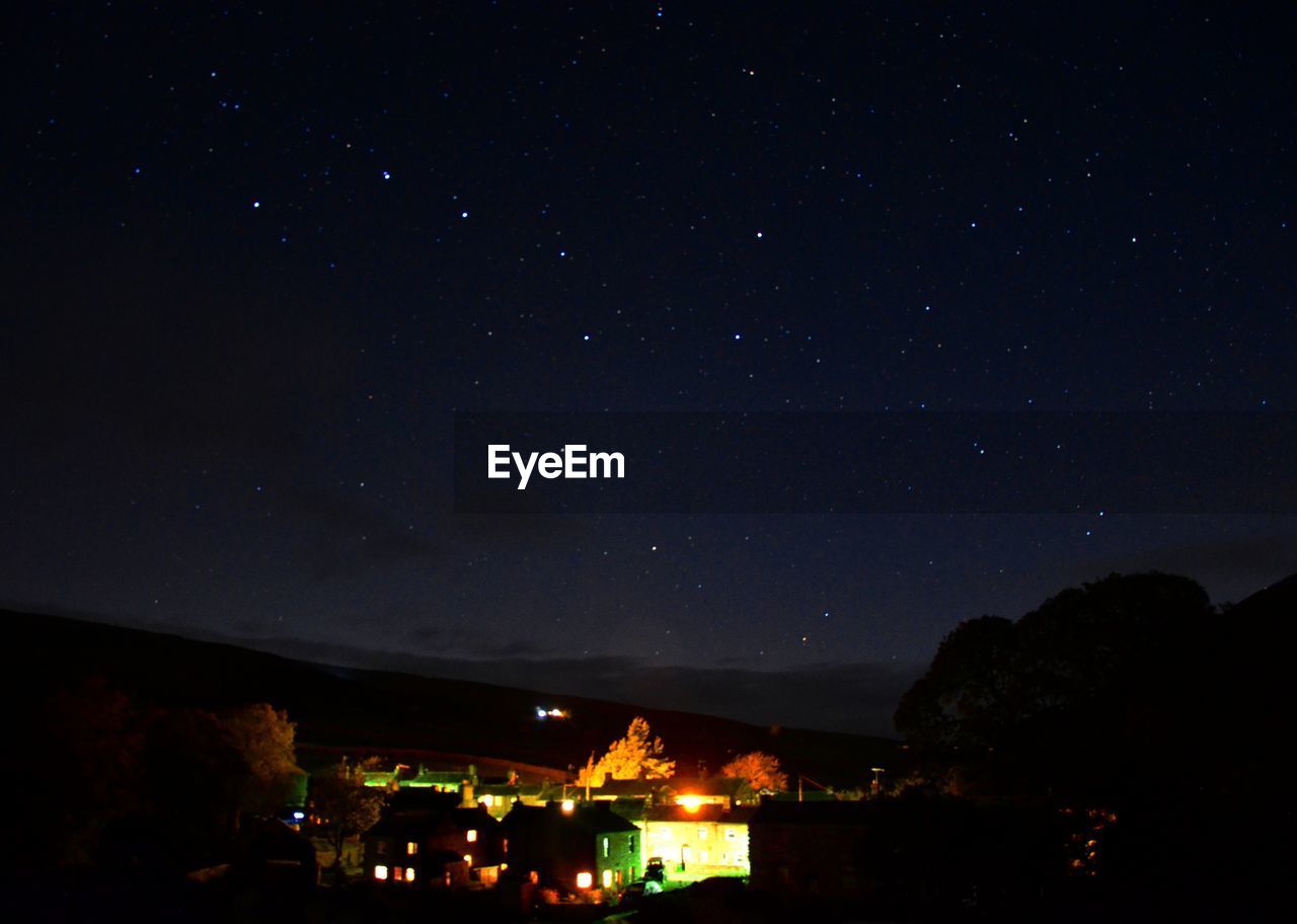 ILLUMINATED SKY OVER SILHOUETTE FIELD AGAINST STAR TRAILS