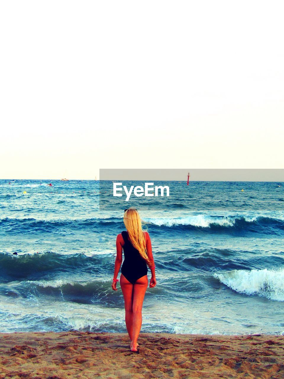 Rear view of young woman walking at beach against clear sky during sunset