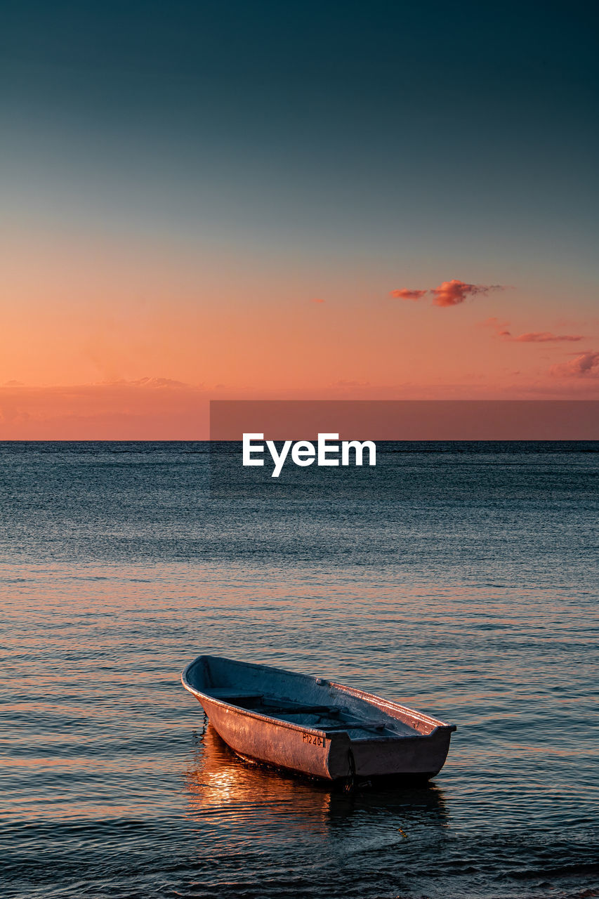 Boat moored on sea against sky during sunset