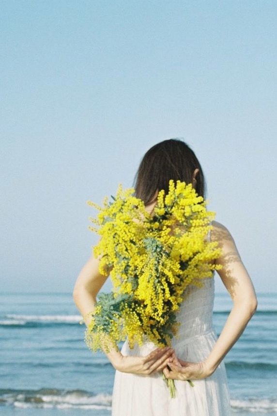yellow, nature, flowering plant, flower, sea, one person, water, sky, plant, flower arrangement, women, bouquet, adult, beauty in nature, standing, clear sky, female, horizon over water, beach, dress, young adult, day, holding, bride, horizon, land, outdoors, hairstyle, waist up, three quarter length, copy space, emotion, blue, rear view, clothing, leisure activity, person, sunny, spring, lifestyles, wedding dress, portrait, long hair