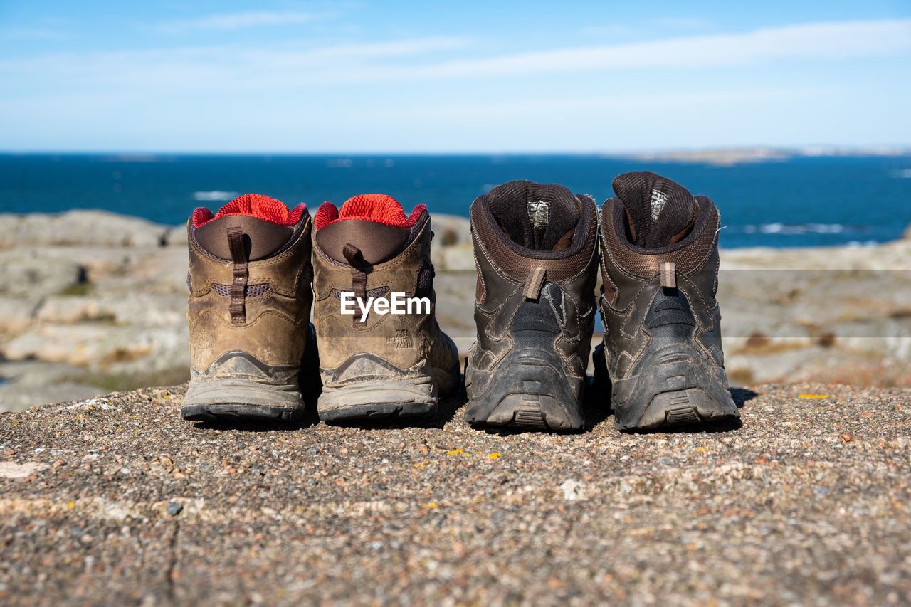footwear, shoe, sand, land, nature, sea, beach, pair, water, day, sky, outdoors, in a row, no people, horizon over water, natural environment, rock, blue, shore, boot, coast