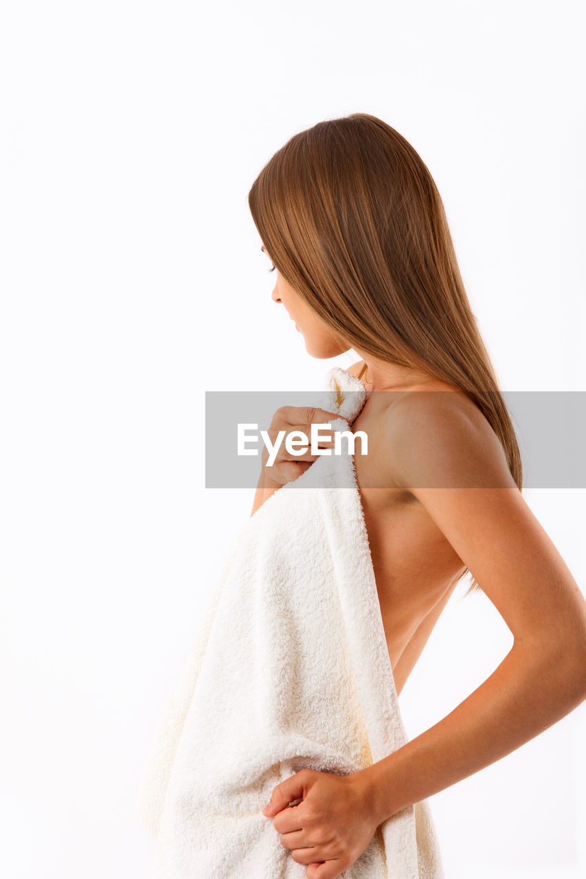 Naked young woman covered in towel standing against white background