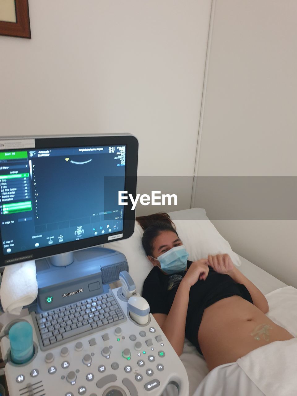 YOUNG WOMAN USING MOBILE PHONE WHILE SITTING ON BED IN BEDROOM