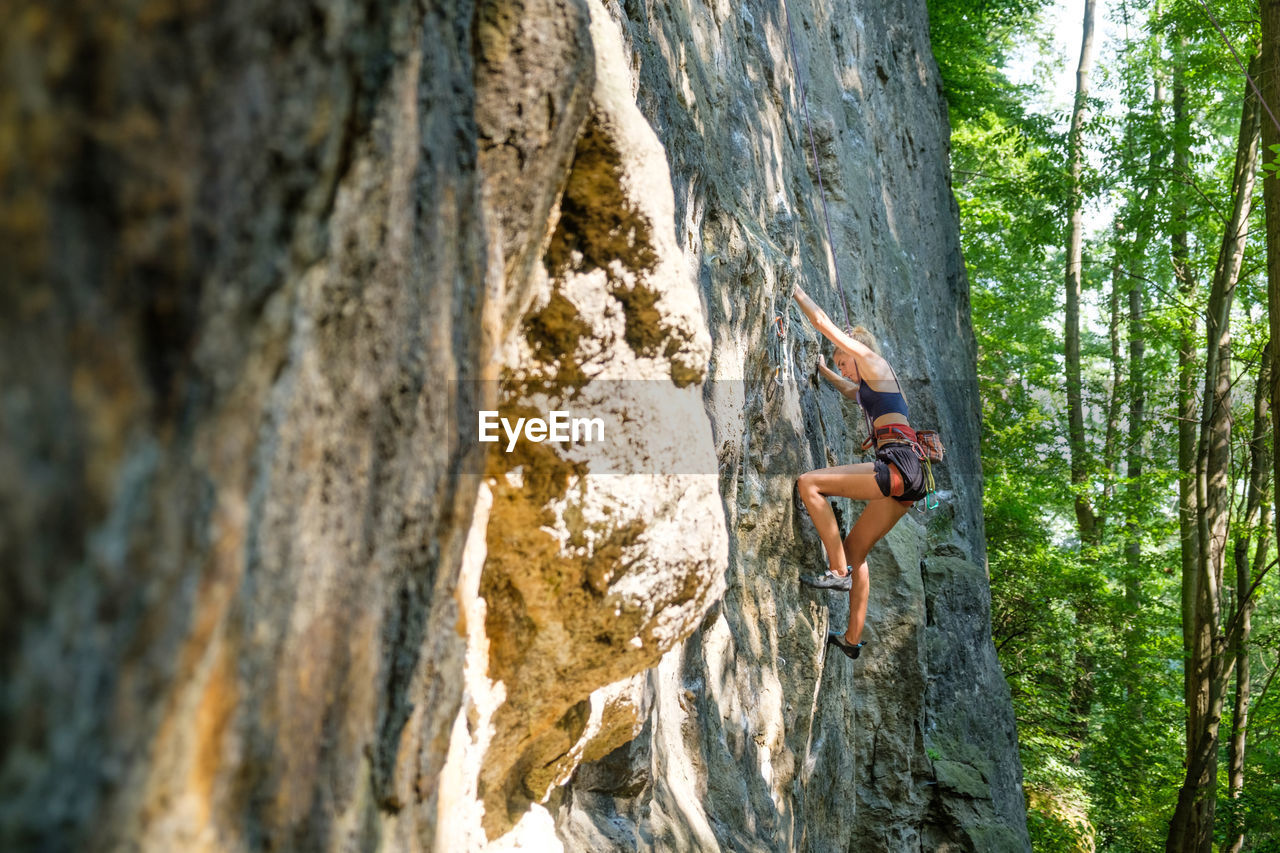 Low angle view of woman rock climbing on wall outdoors