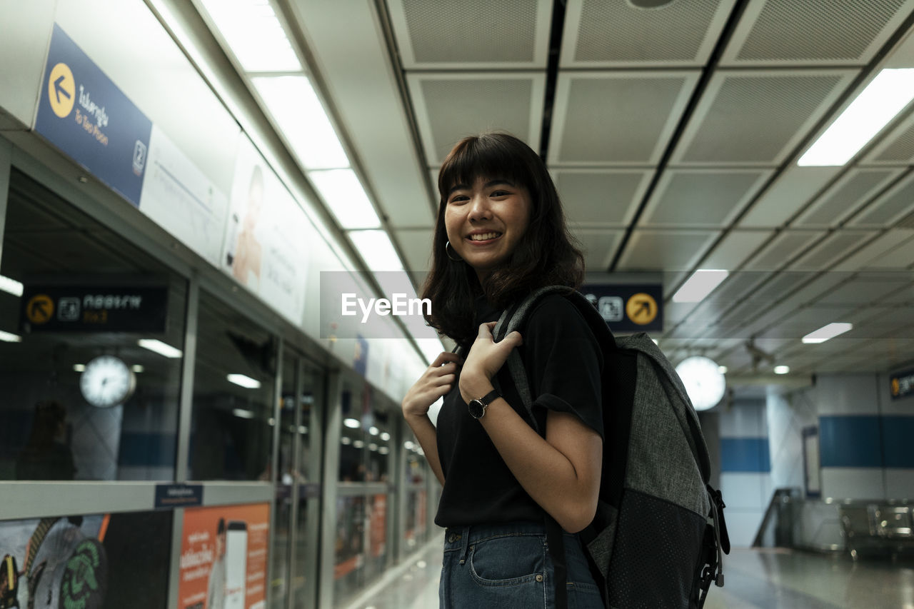 PORTRAIT OF A SMILING YOUNG WOMAN STANDING AT HOME