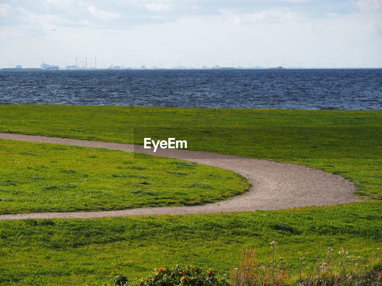 Scenic view of field by sea against sky