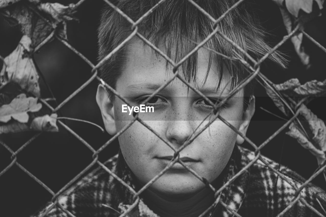 Close-up of boy standing by chainlink fence