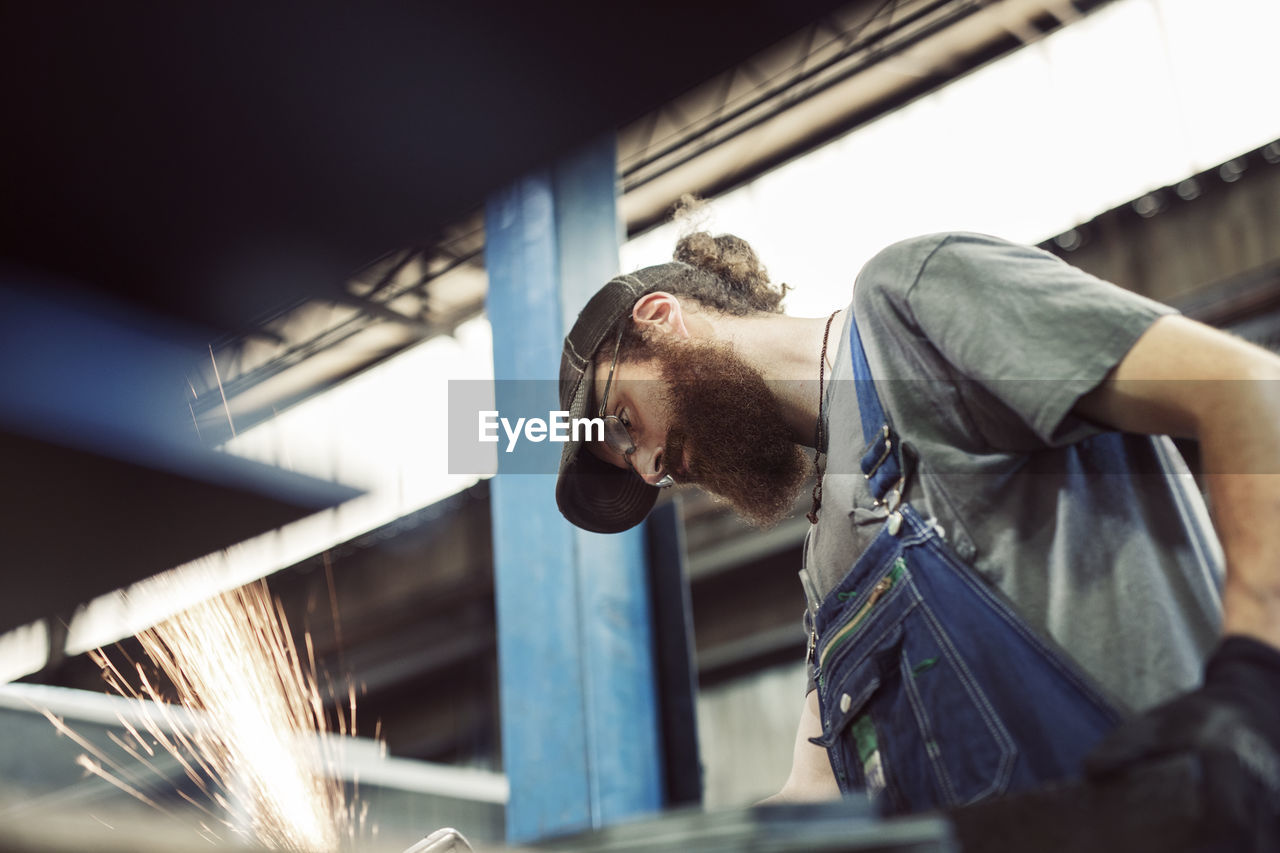 Low angle view of blue collar worker using welding machine in steel industry