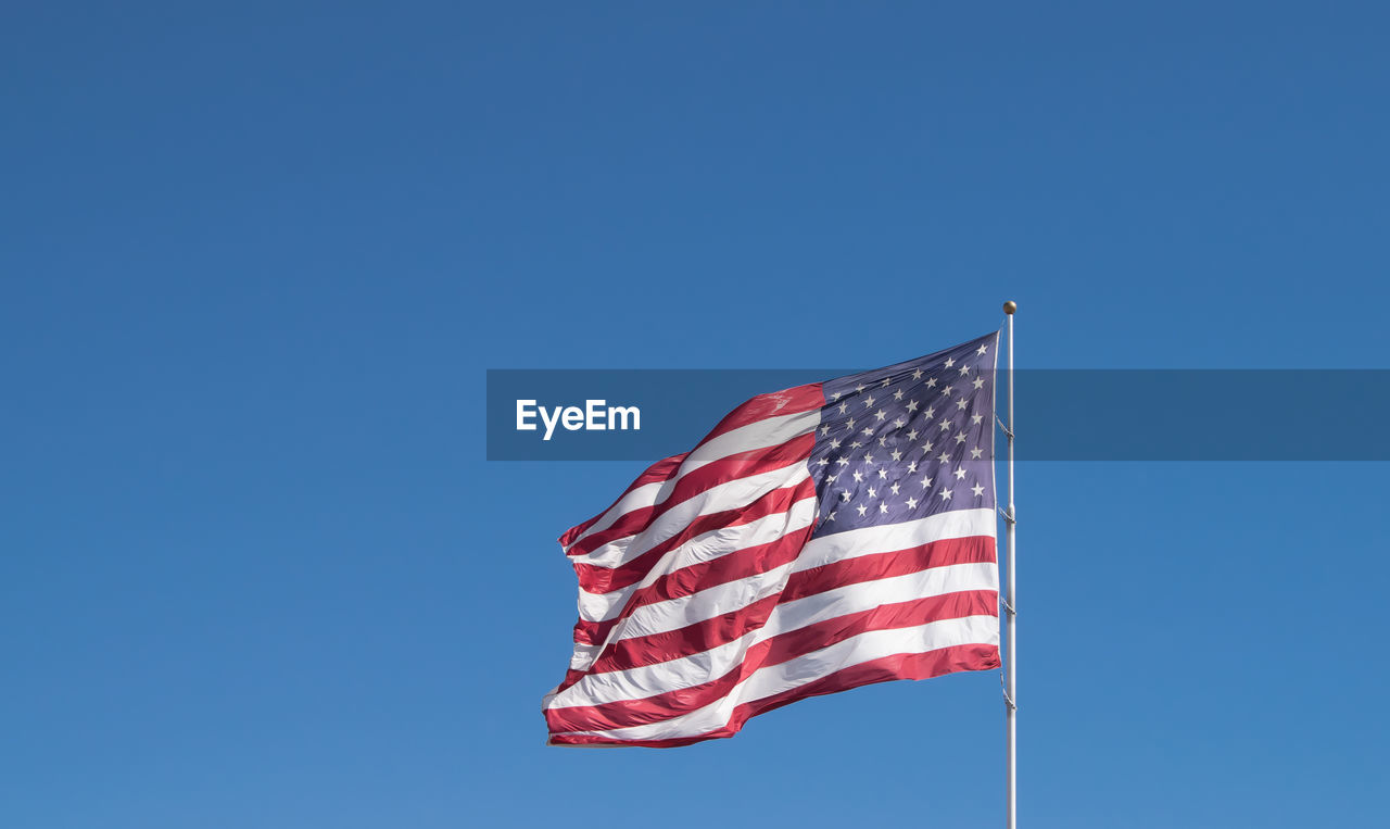 Low angle view of american flag waving against clear blue sky