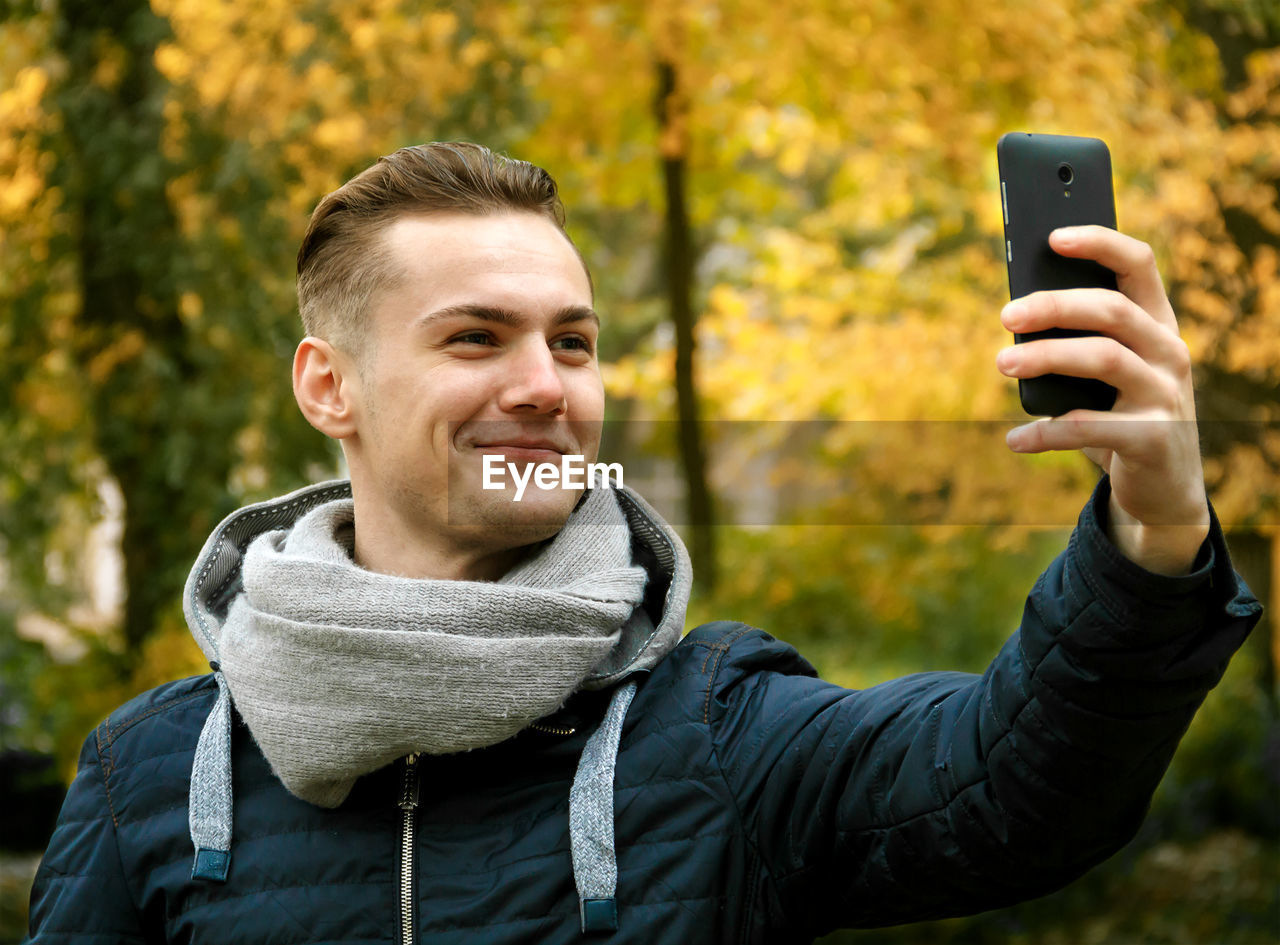 Cute young man with smartphone in autumn park