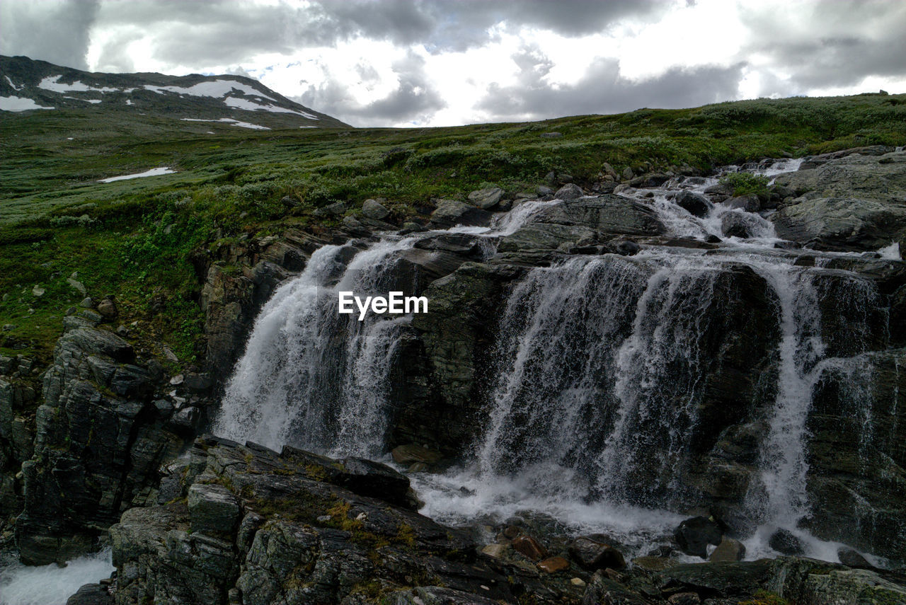 SCENIC VIEW OF WATERFALL AGAINST CLOUDY SKY