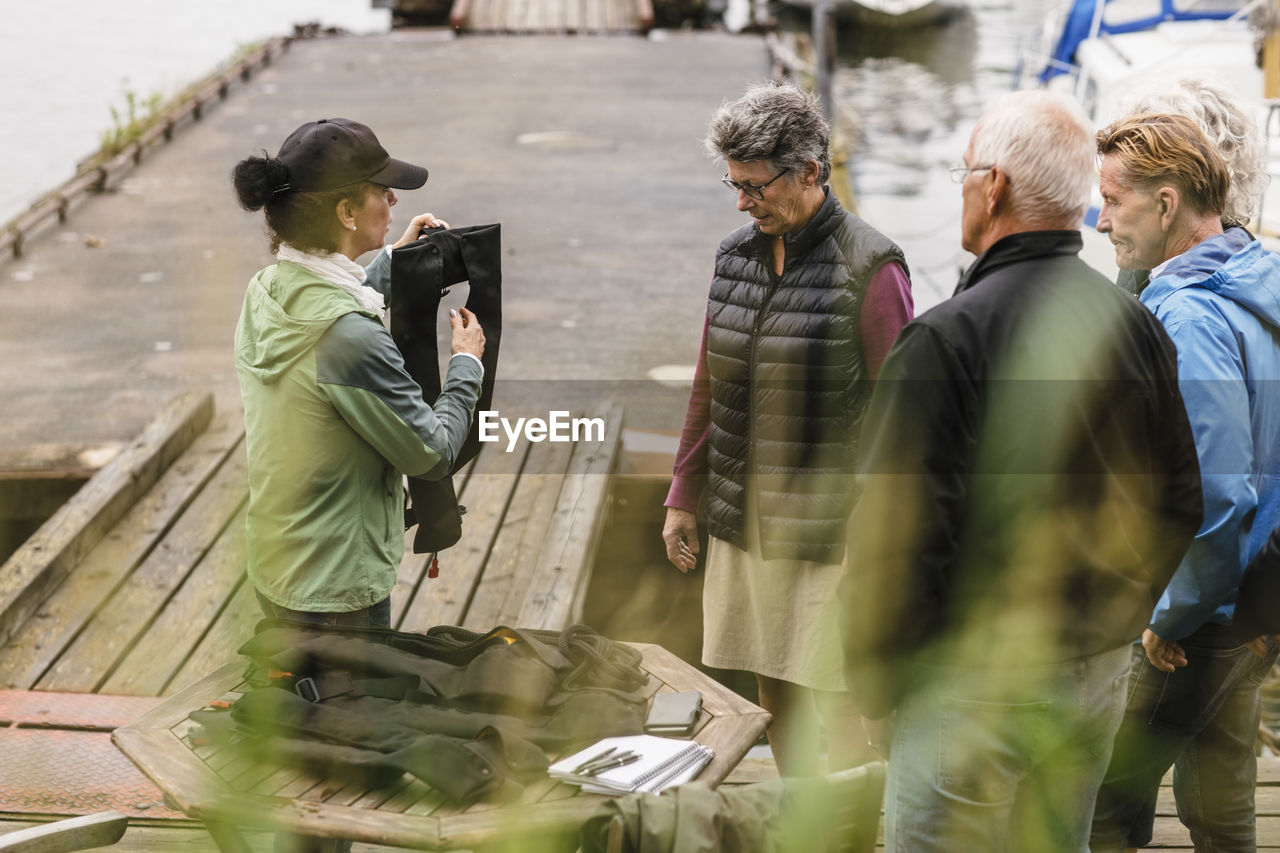 Female instructor explaining senior men and woman about life jacket during boat master course