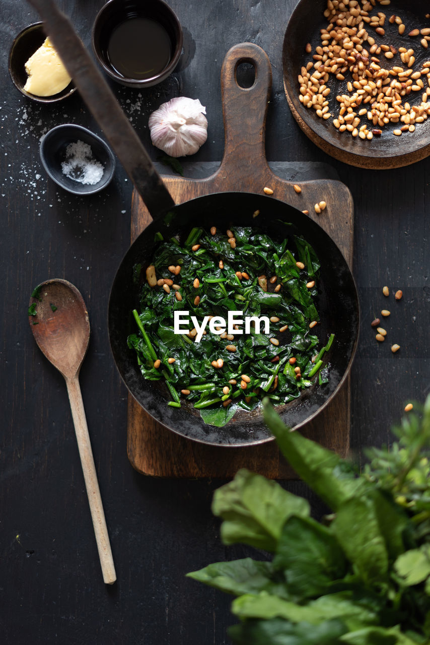 From above of tasty catalan spinach with pine nuts in frying pan served on table in kitchen