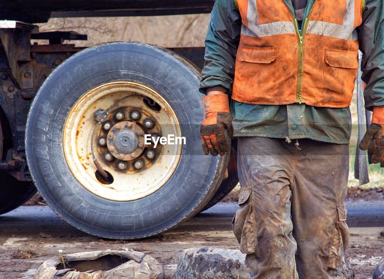 Midsection of construction worker walking against truck