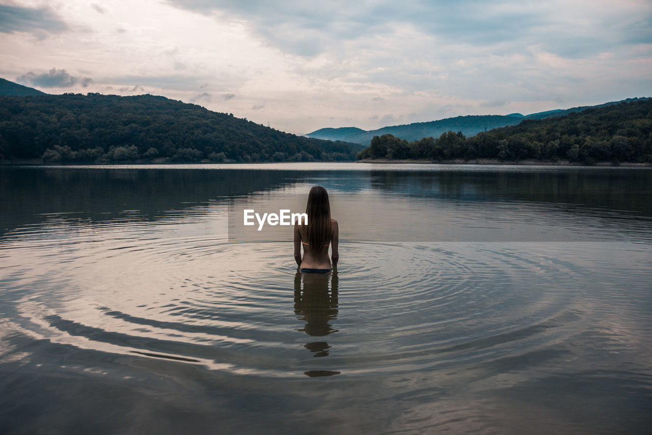 Young woman standing in lake against sky during sunset