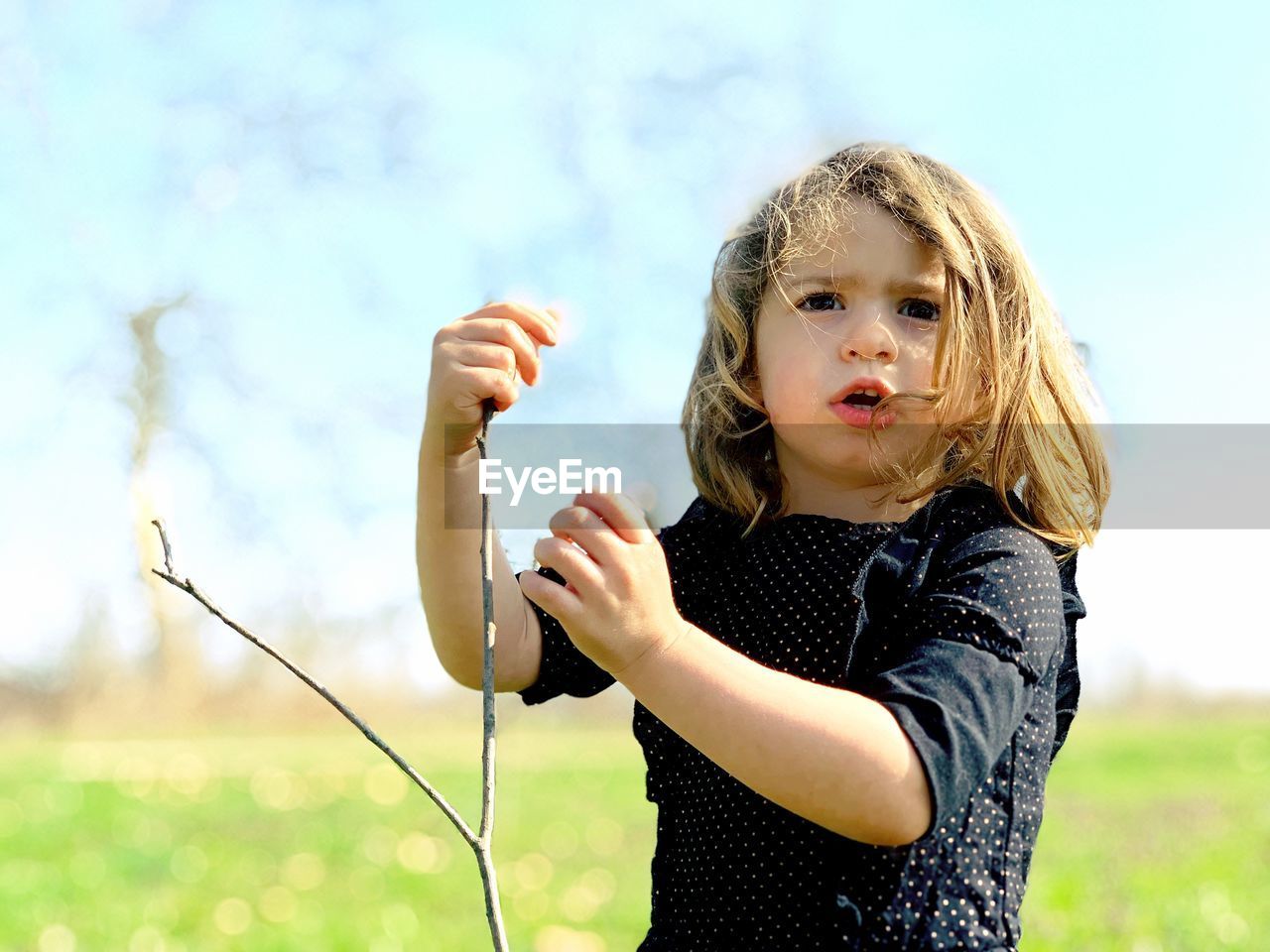 Cute girl looking away while holding stick on land