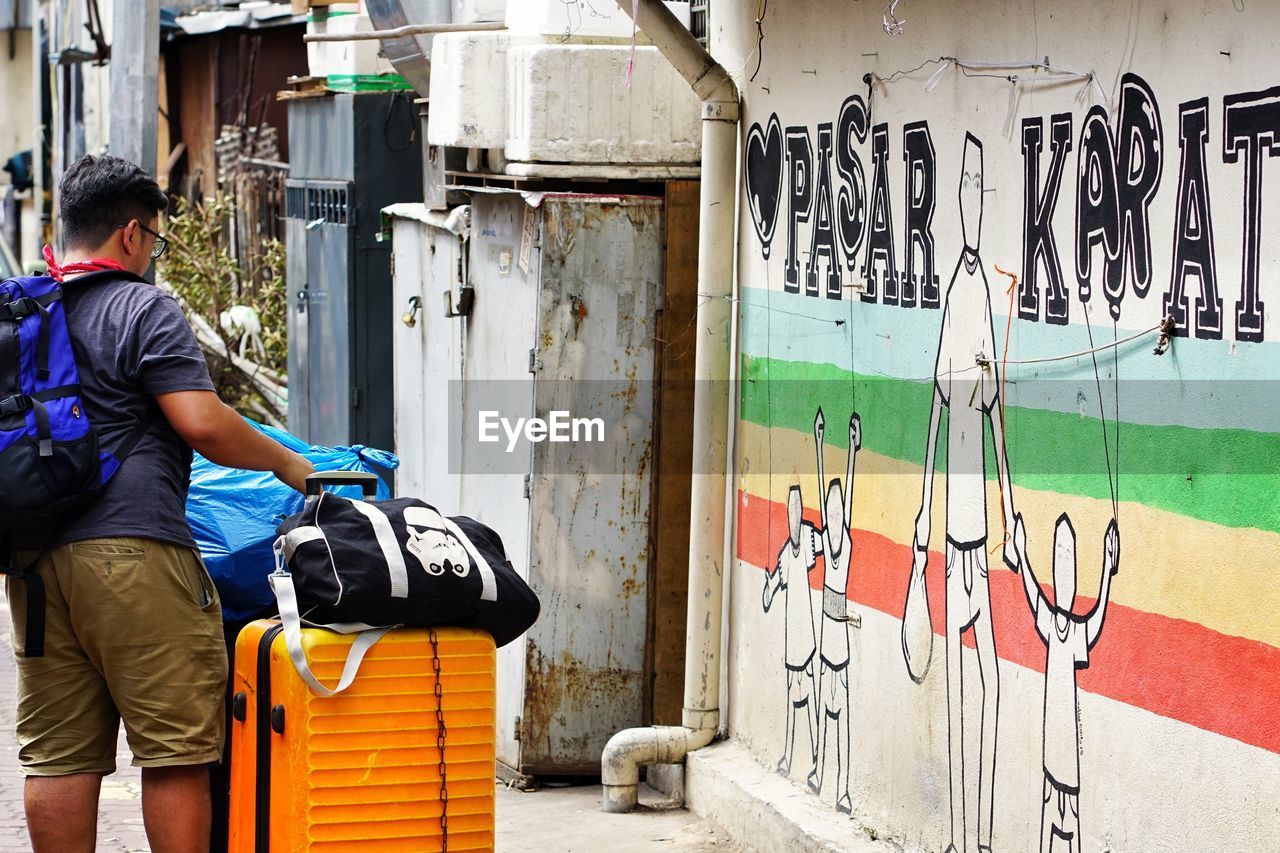 REAR VIEW OF MAN STANDING BY GRAFFITI