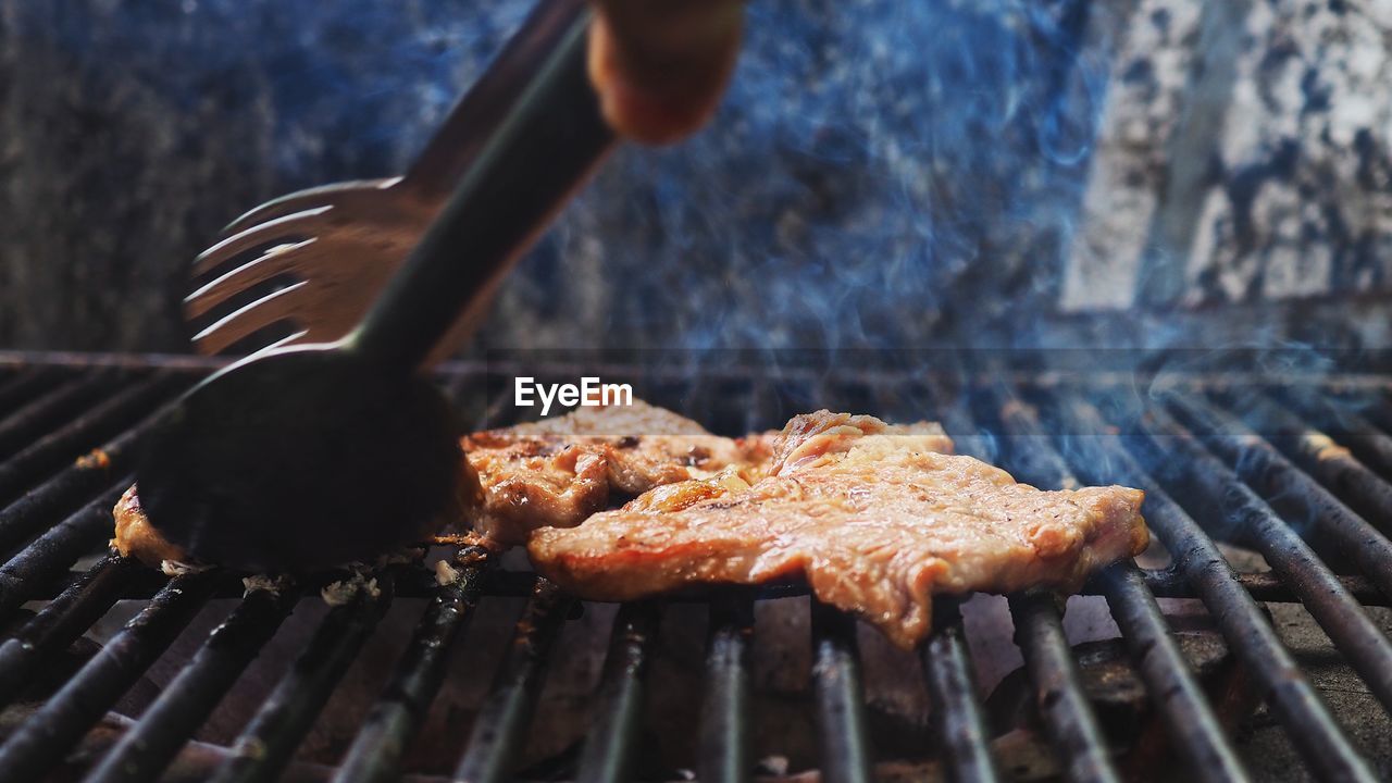 Close-up hand preparing meat on barbecue grill