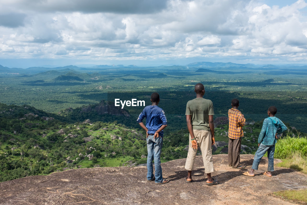 REAR VIEW OF PEOPLE STANDING ON MOUNTAIN AGAINST SKY