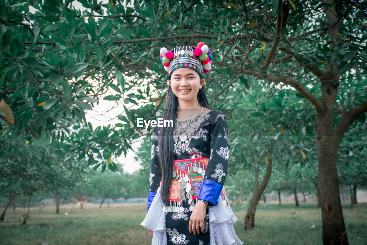 PORTRAIT OF A SMILING YOUNG WOMAN STANDING OUTDOORS