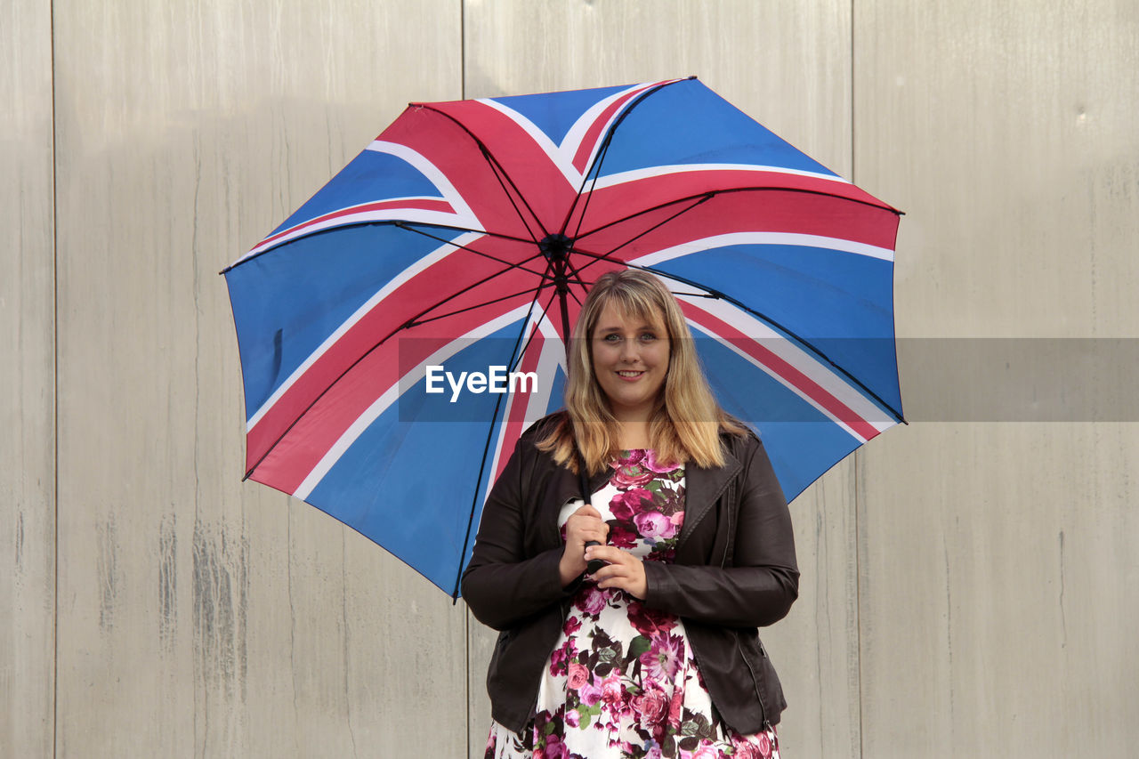 Young woman carrying british flag patterned umbrella against wall