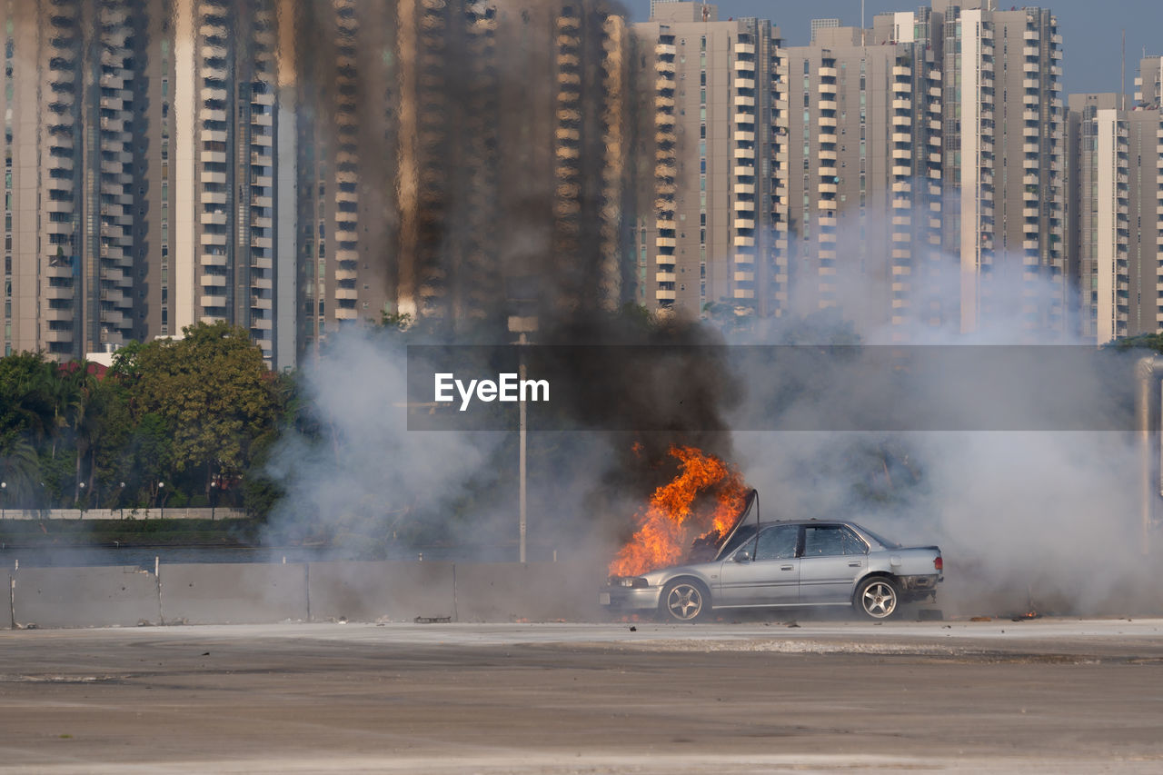 Burning car on road against buildings in city