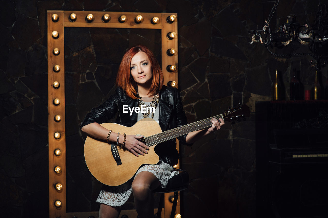 FULL LENGTH PORTRAIT OF WOMAN PLAYING GUITAR IN MUSIC CONCERT