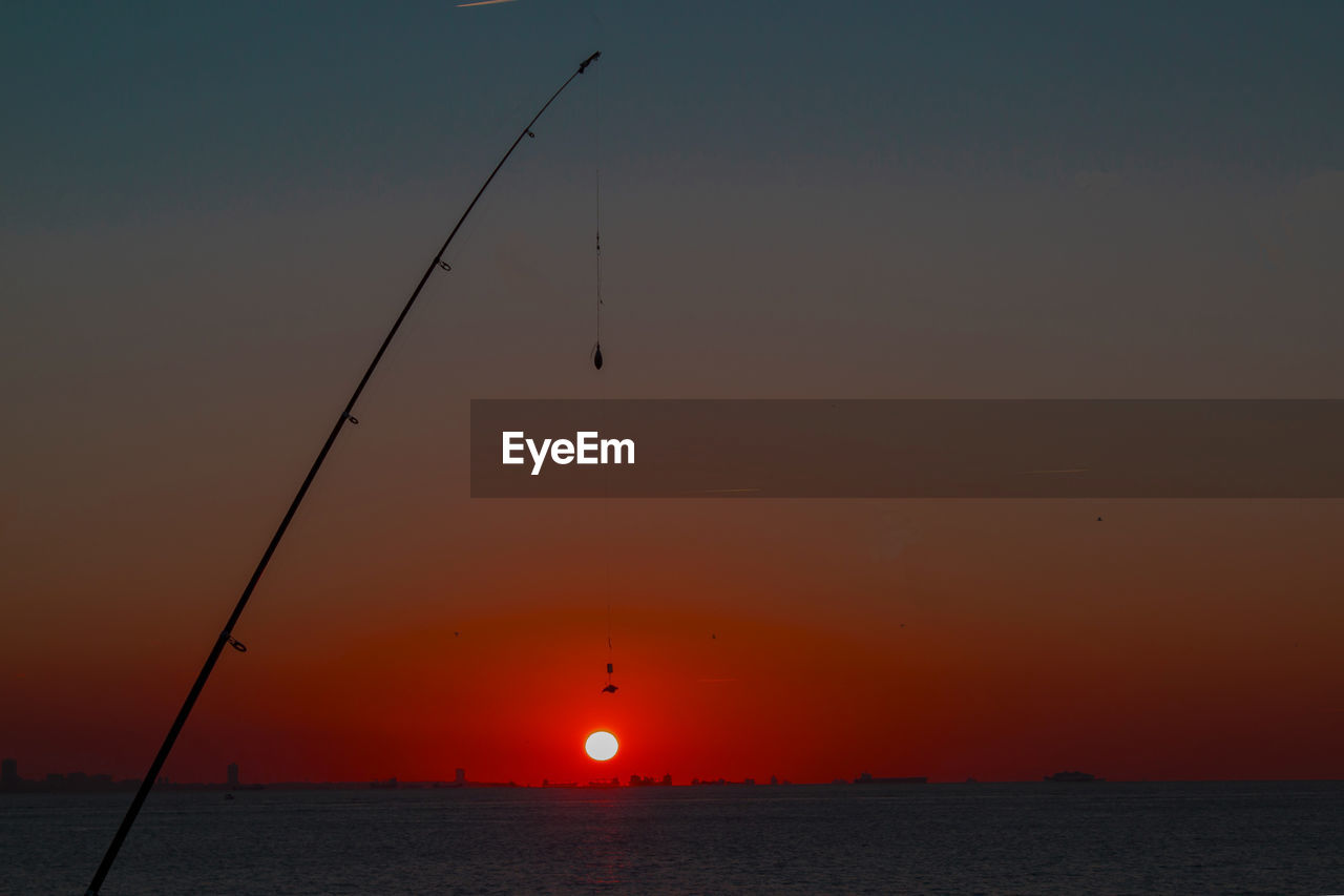 Low angle view of silhouette fishing rod by lake against sky during sunset