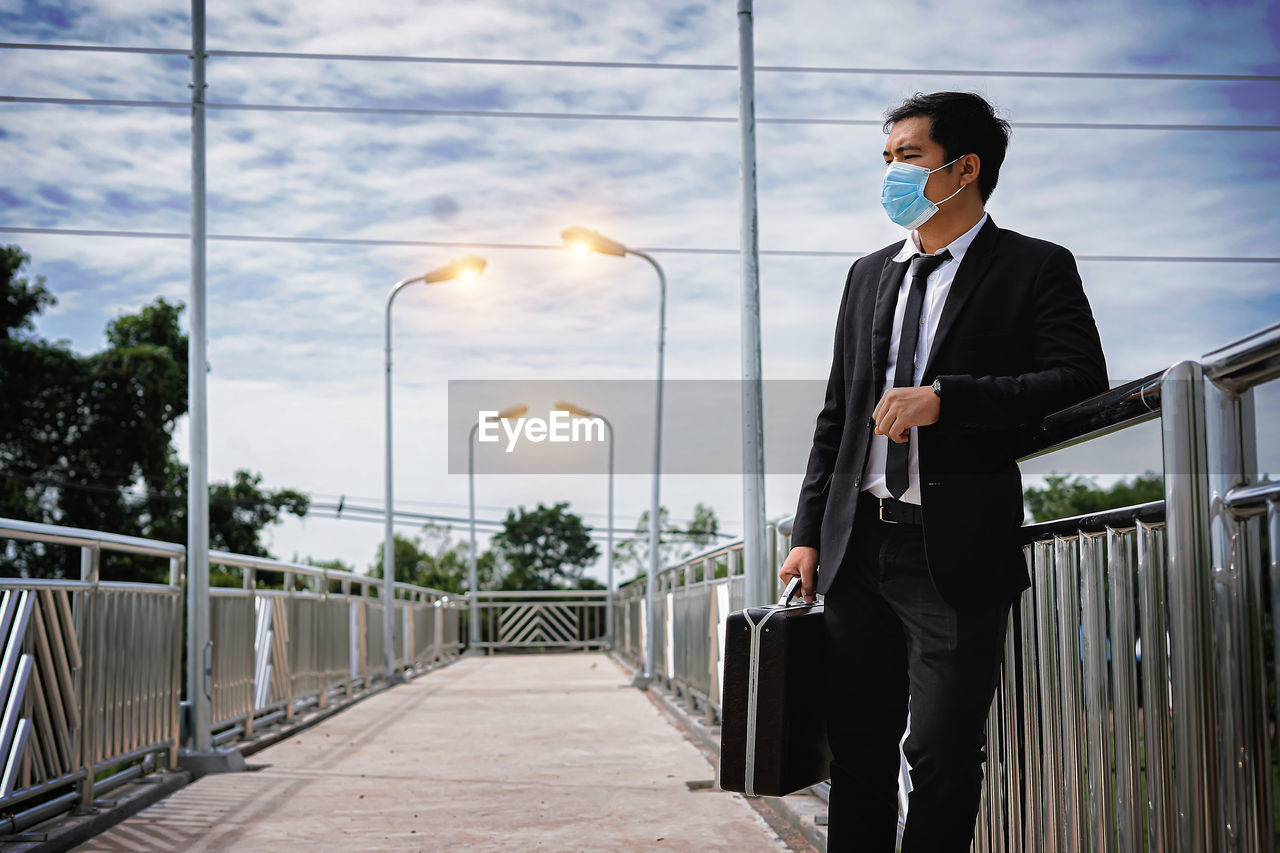 Asian businessman holding briefcase walking on overpass looking outside