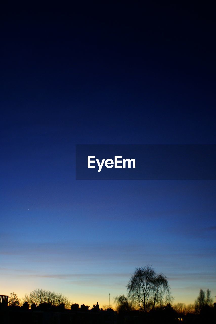 Low angle view of silhouette trees against blue sky