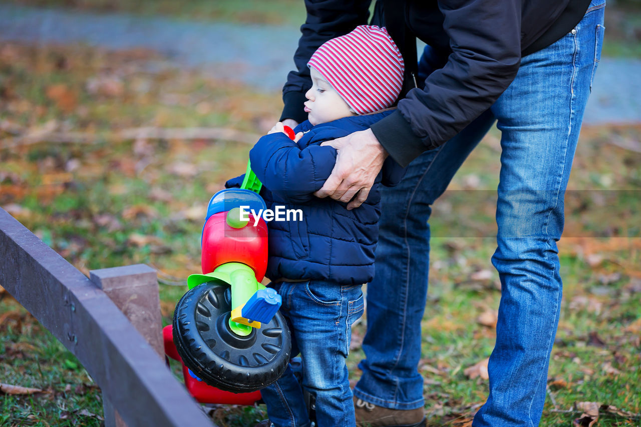 Midsection of father assisting son to carry tricycle