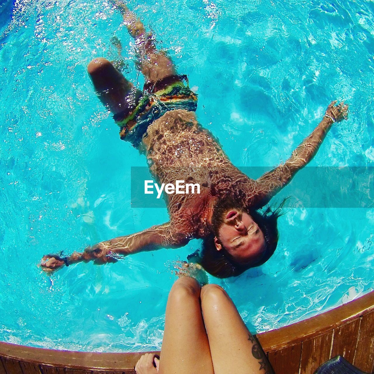 Low section of woman at poolside with man swimming in pool