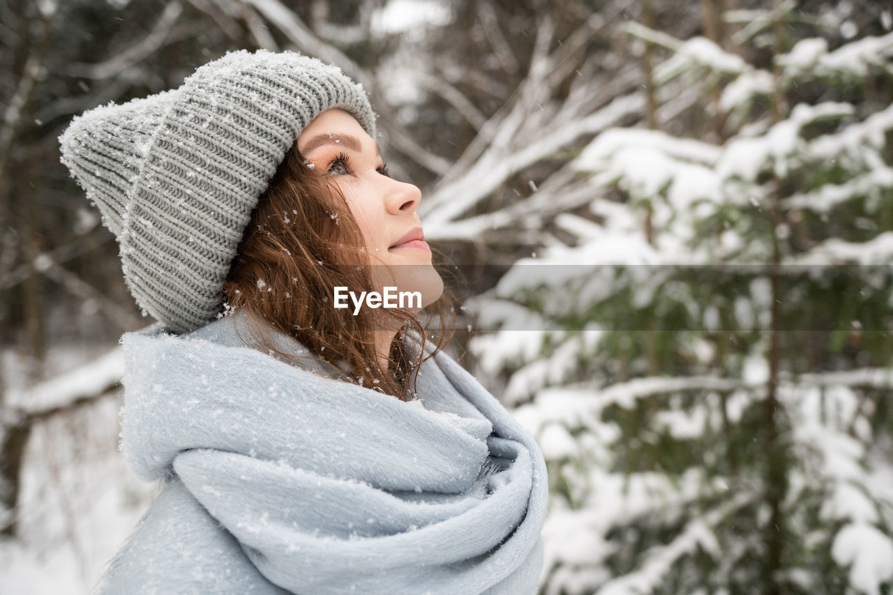 Cute girl in a hat in winter looks up, snowflakes in her hair