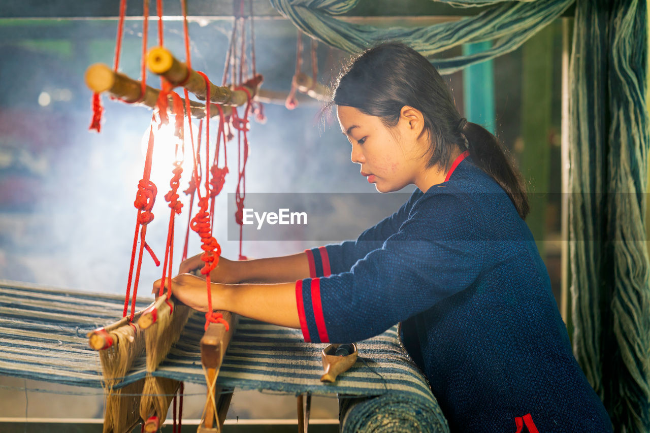 Side view of young woman working at loom