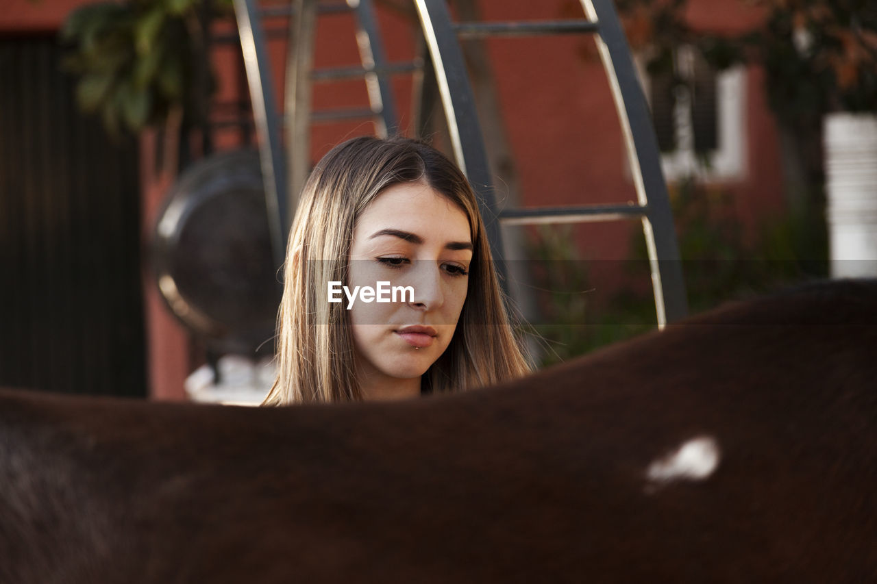 Young blonde woman with her brown horse enjoys a day on the farm.
