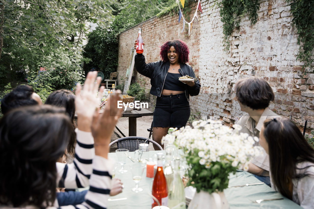 Happy woman with food and drink walking towards friends at dinner party in back yard