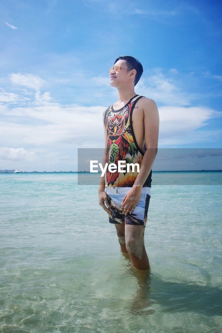 Young man standing in sea against cloudy sky at beach