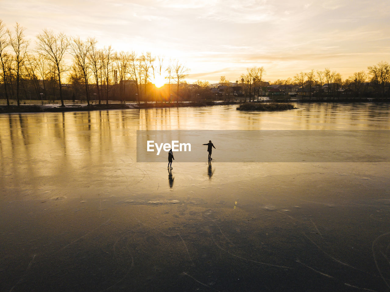 Friends skating on frozen pond during sunset