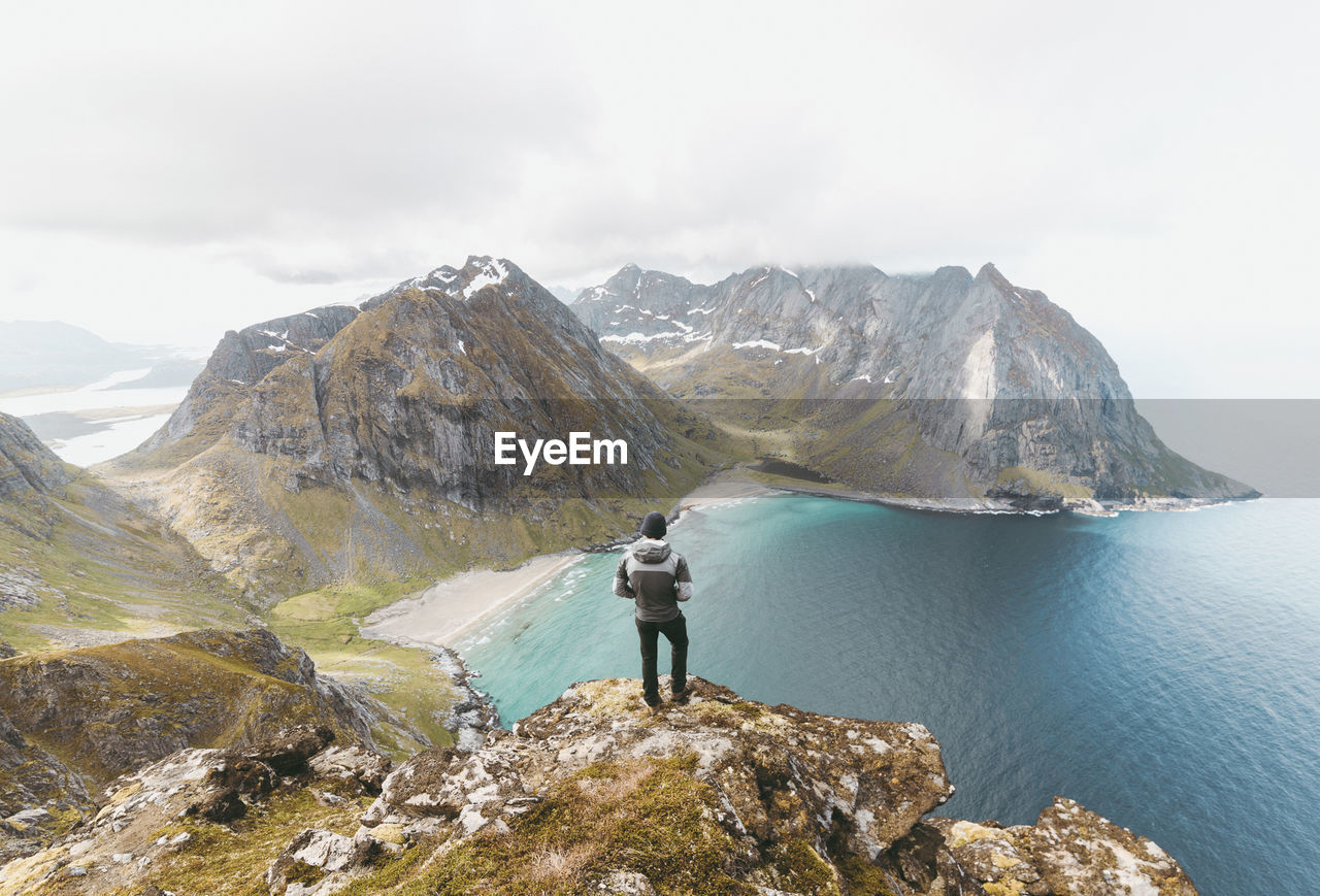 Rear view of man standing on cliff by sea at lofoten archipelago