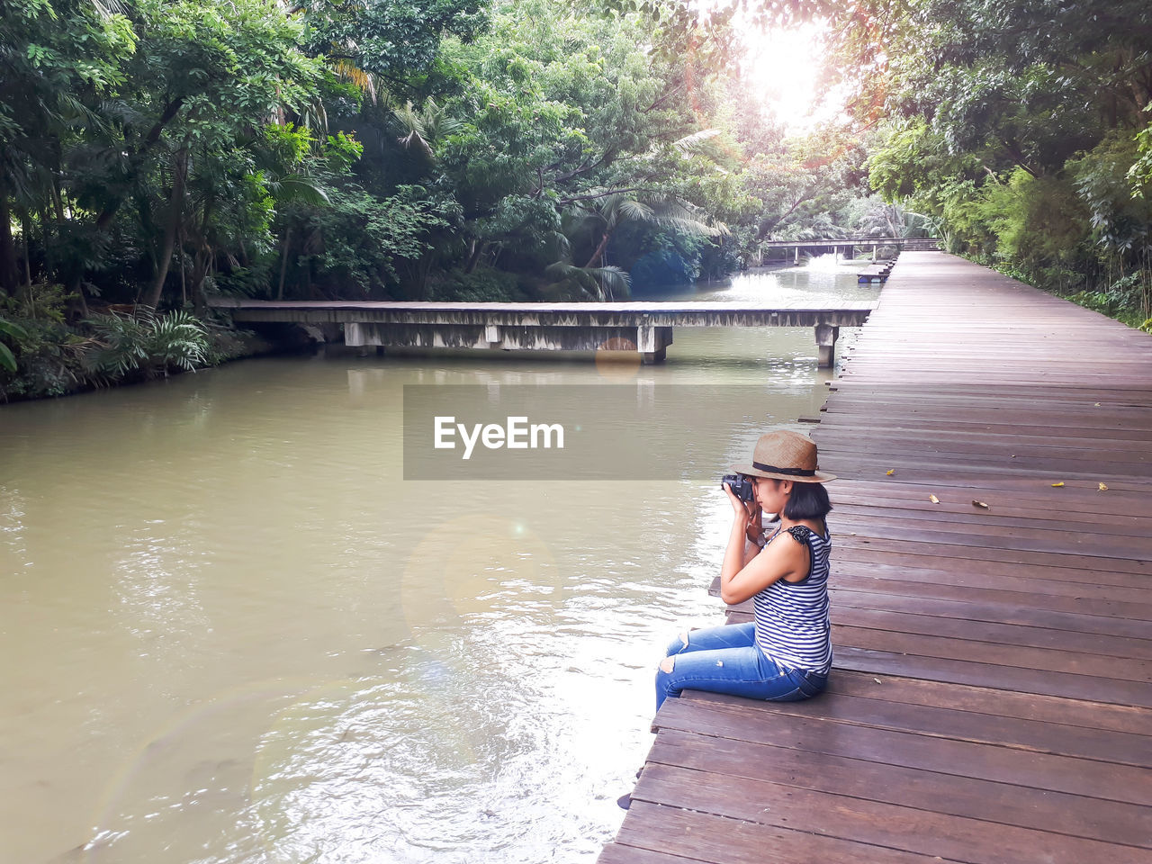 Side view of woman sitting on boardwalk by trees