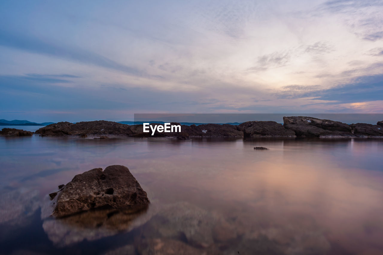 Rocks by sea against sky during sunset