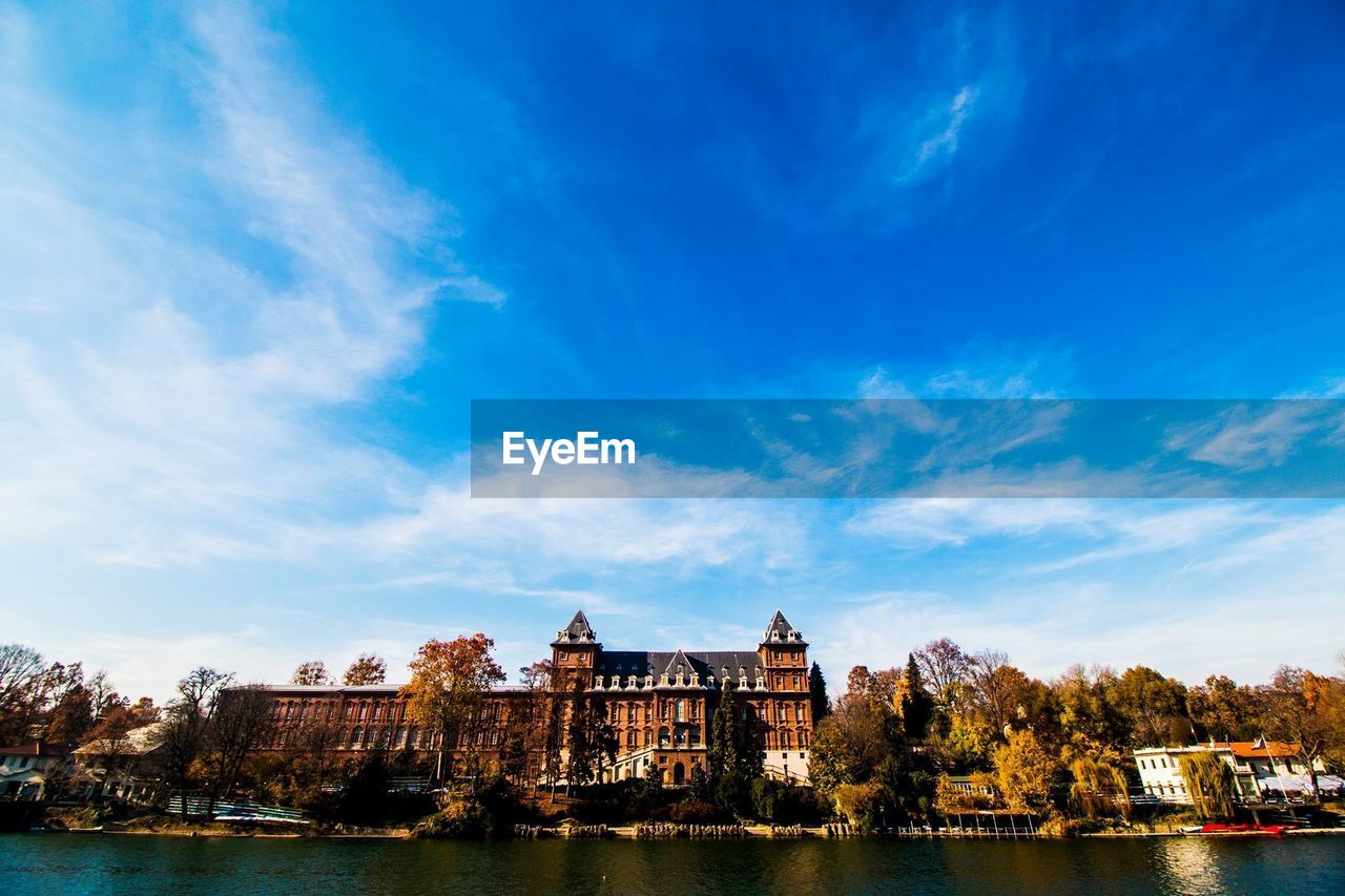 Low angle view of castle in front of river against cloudy blue sky