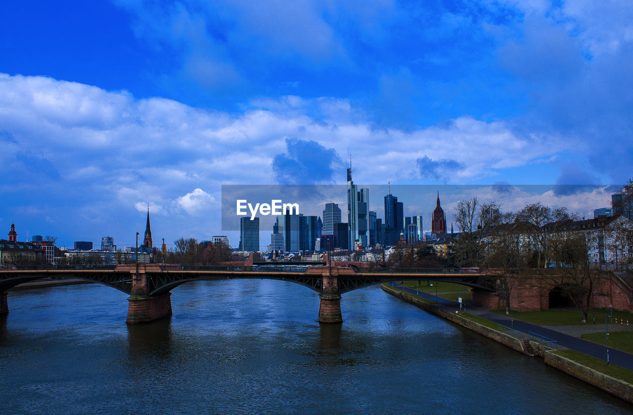 BRIDGE OVER RIVER BY BUILDINGS AGAINST SKY