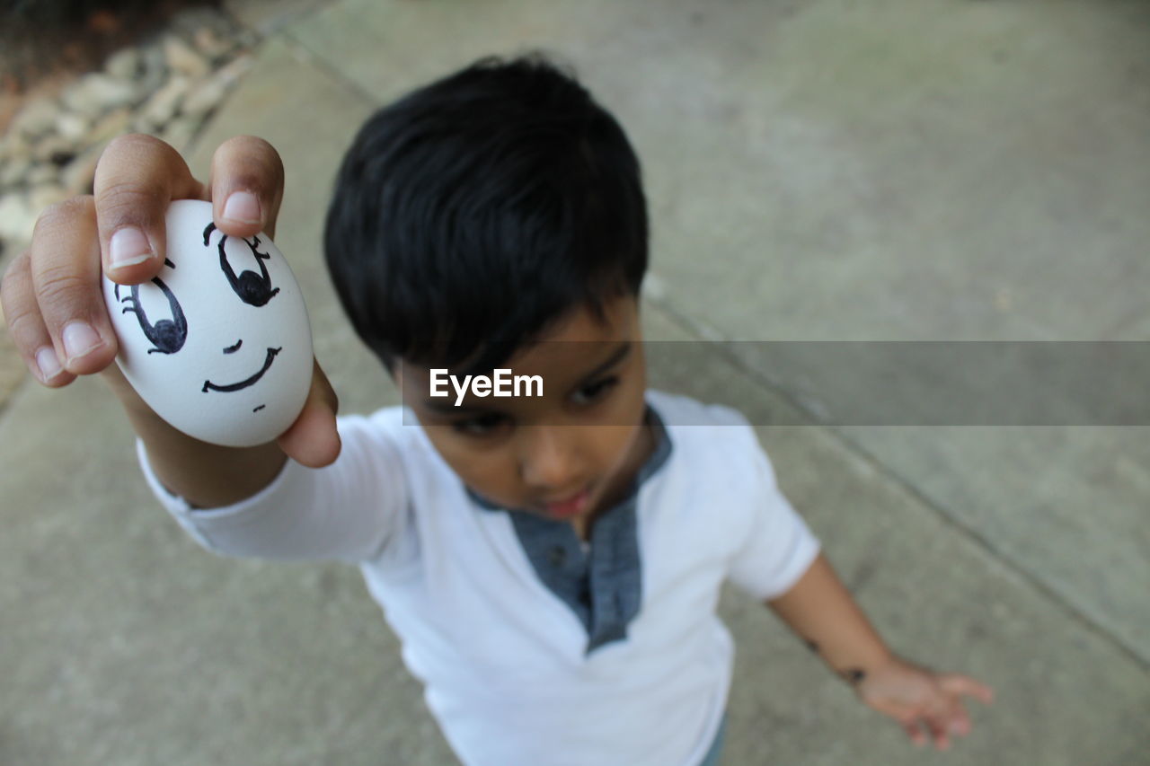 High angle view of boy holding egg with smiley face