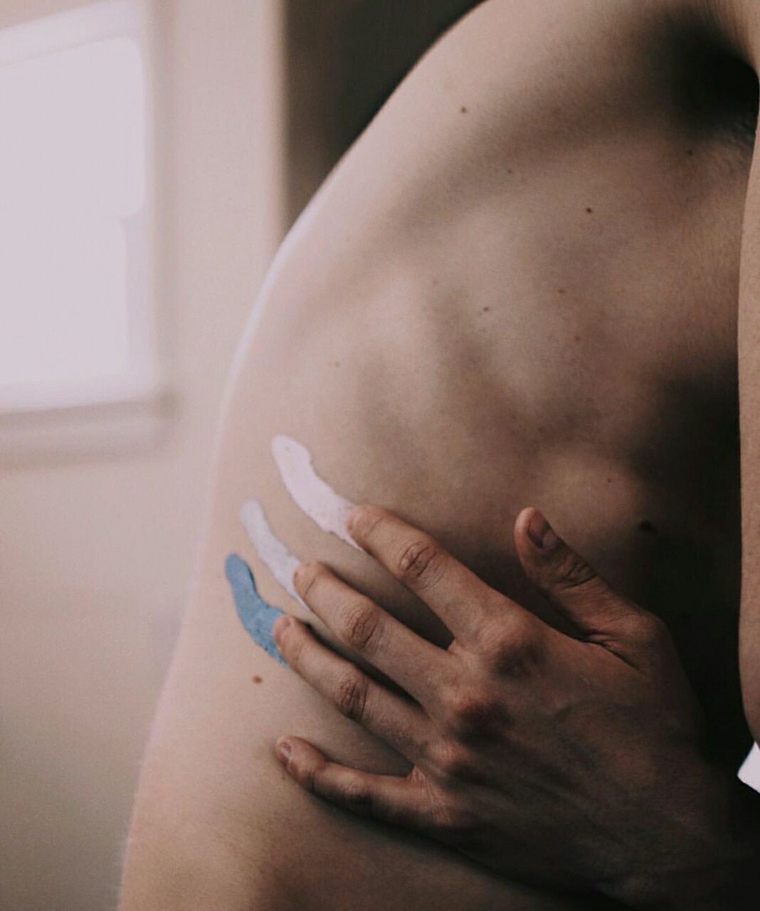 Midsection of shirtless man painting on back at home