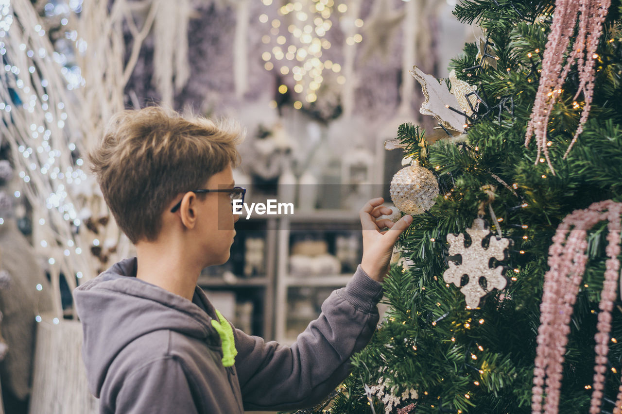 Boy standing by tree while touching christmas decoration at home