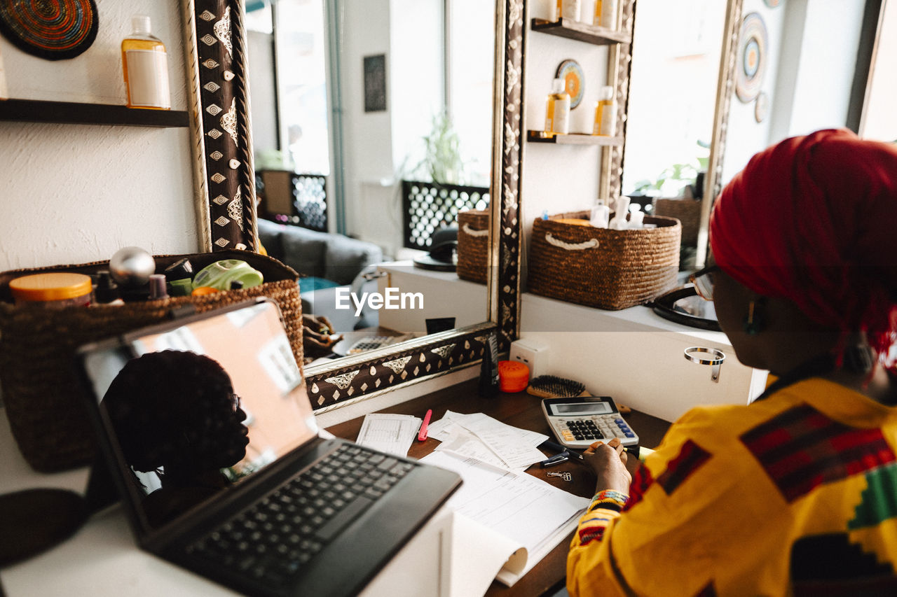 Female hairdresser with laptop at table in barber shop