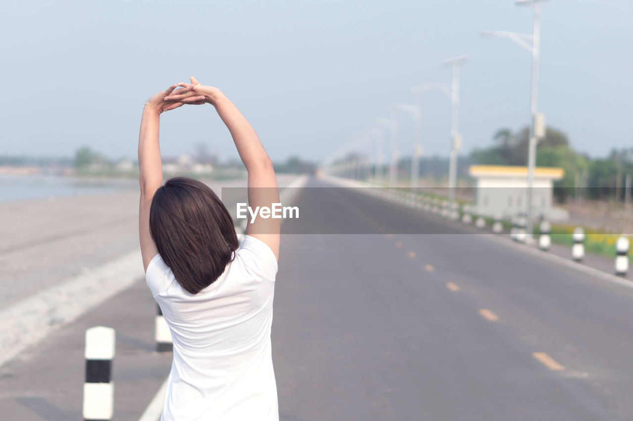 REAR VIEW OF WOMAN STANDING BY ROAD