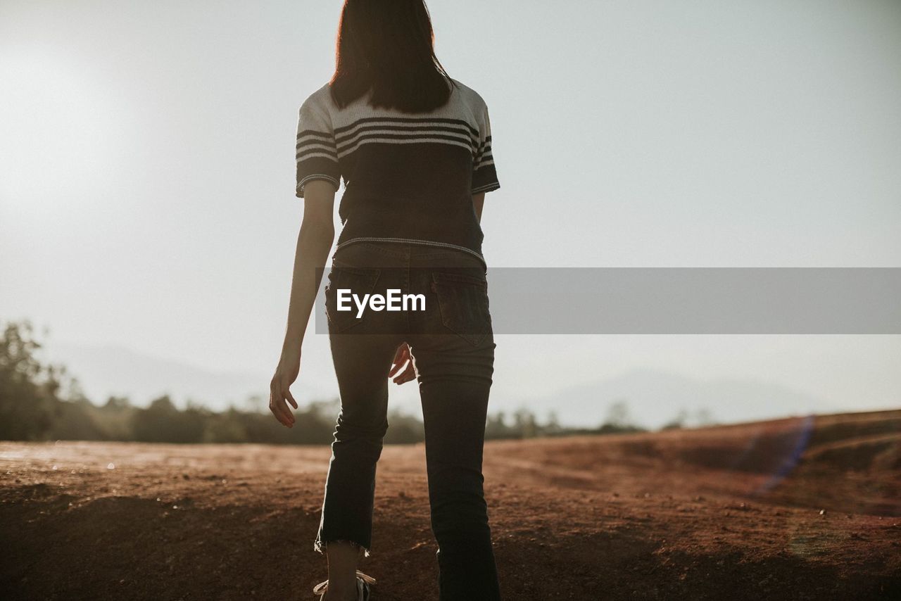 Rear view of young woman walking on field against clear sky