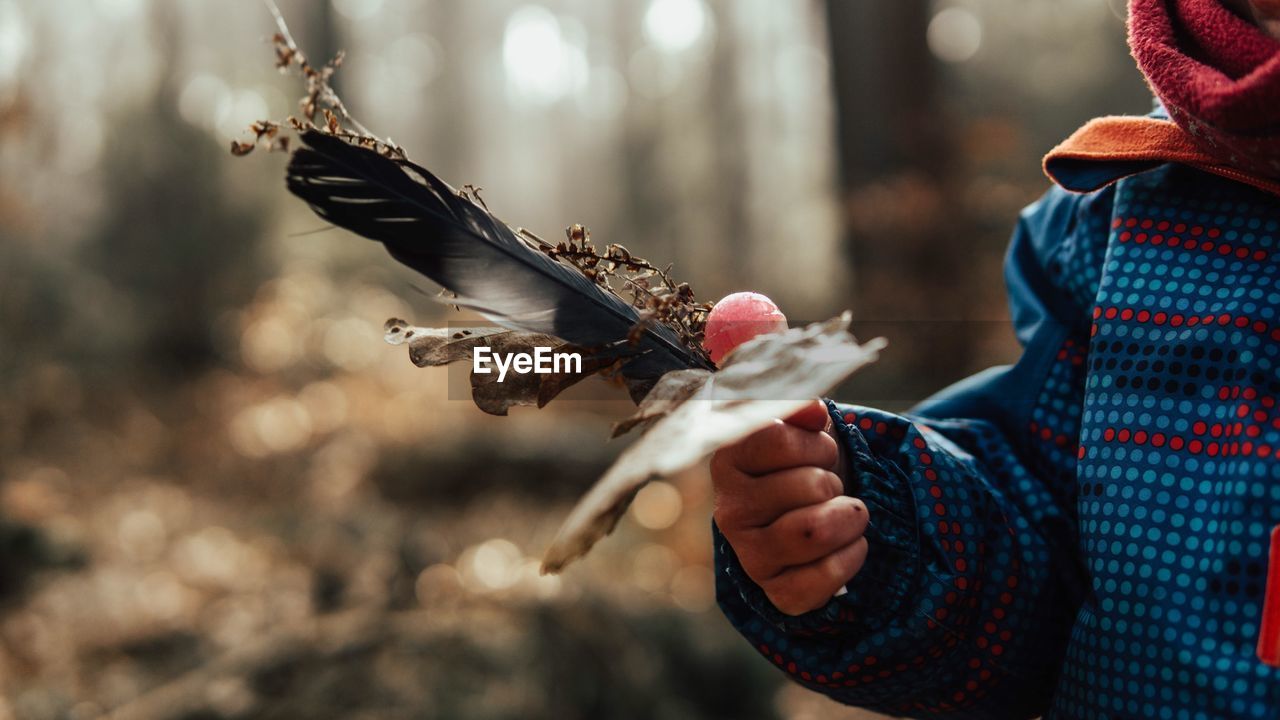 Midsection of kid holding dry leaf with feather in forest